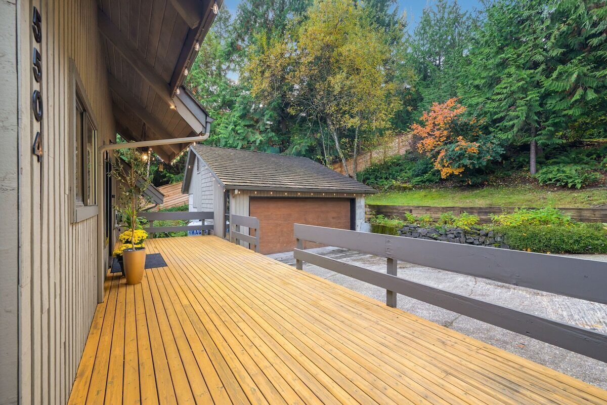 Una terraza de madera con un banco, un cobertizo pequeño y un muro de piedra en un jardín.