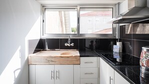 Una cocina moderna con encimera de mármol, armarios blancos, salpicadero negro y ventana con vistas a edificios.
