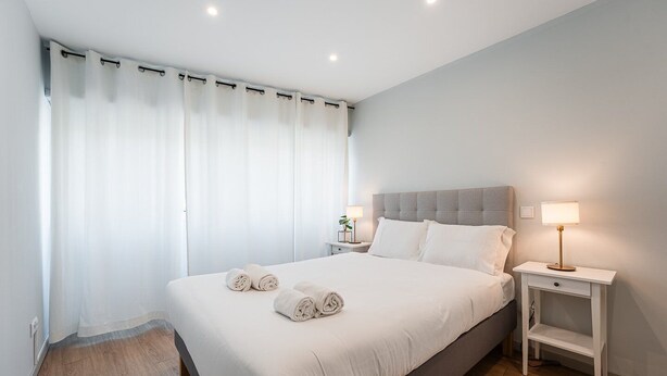Una habitación de hotel moderna con una cama grande, dos mesitas de noche y una mesita auxiliar.