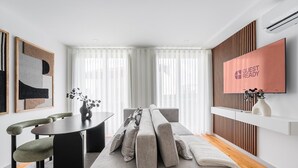 A modern living room with a grey sofa, a dining table with chairs, and a TV mounted on the wall. - GuestReady - Urban elegance in Porto (Porto)