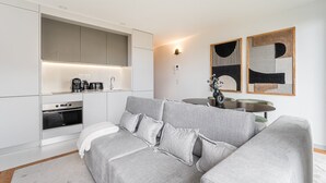 A modern kitchen with integrated appliances, a grey sofa, and abstract wall art. - GuestReady - Urban elegance in Porto (Porto)