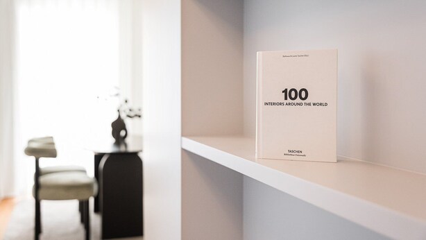 A book titled "100 Interiors Around the World" on a white shelf in a modern, minimalistic room with a chair and a small table. - GuestReady - Urban elegance in Porto (Porto)