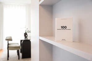 A book titled "100 Interiors Around the World" on a white shelf in a modern, minimalistic room with a chair and a small table.