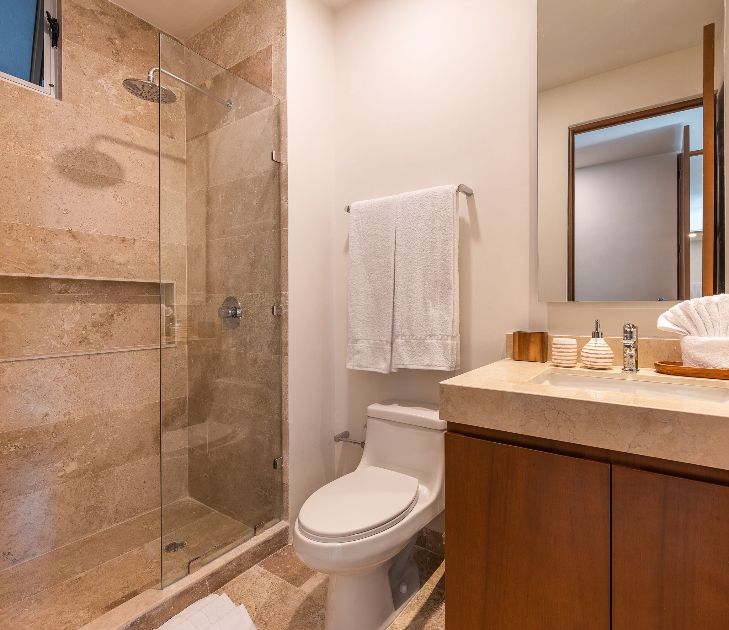 A modern bathroom with a glass-enclosed shower, a toilet, and a vanity with a mirror and sink.