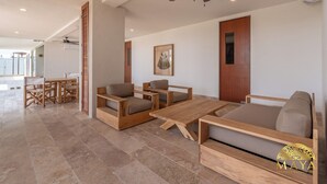 A spacious living area with a wooden sofa, a coffee table, and a dining set. - NHOA 309C Lux 1BR Pool View  Aldea Zama (Tulum)