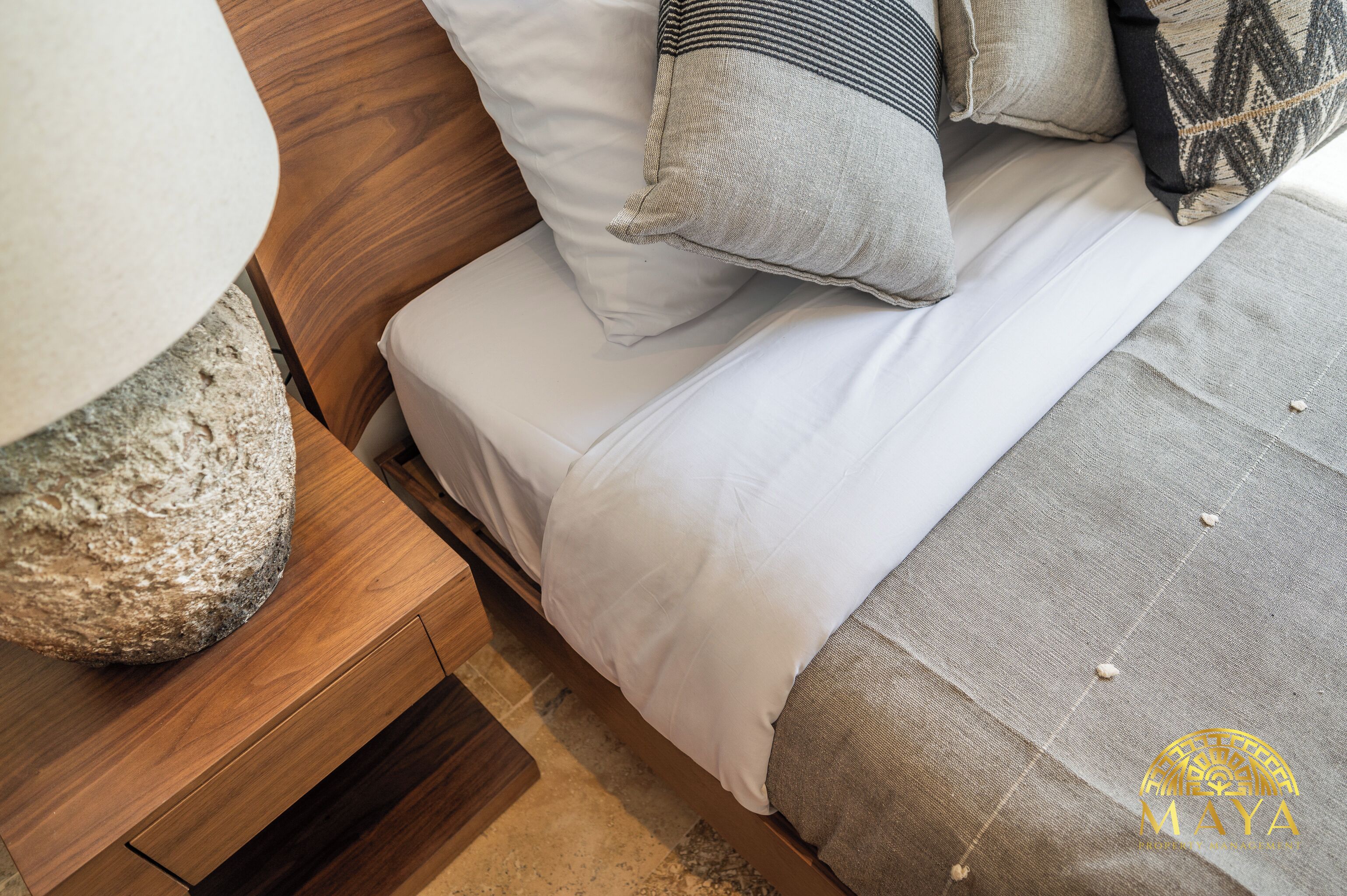 A bed with white bedding, a wooden nightstand, and a large stone vase.
