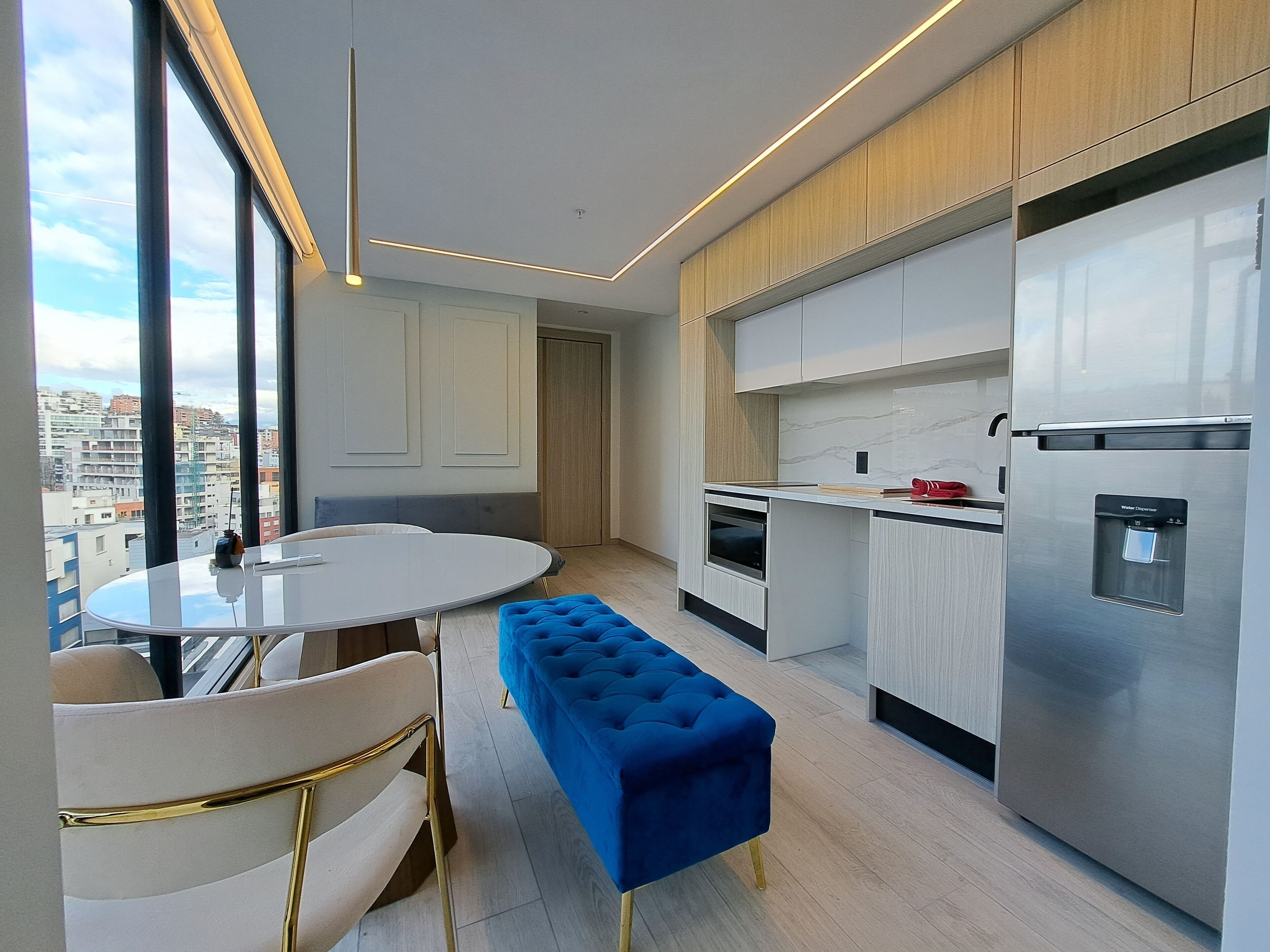 A modern kitchen with a built-in oven, a water dispenser, and a dining area with a round table and chairs.