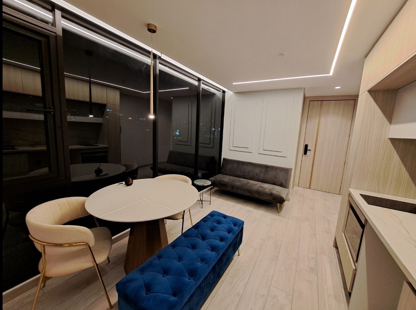 Een modern interieur met een ronde eettafel, twee stoelen, een blauwe bank, een bank en een keukenhoek.