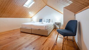 A bedroom with a sloped ceiling, a bed with white bedding, a chair, and a small table with a lamp. - GuestReady - Charming mezzanine near Porto (Vila Nova de Gaia)
