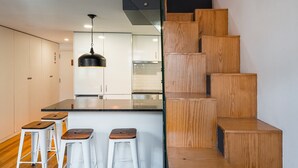 A modern kitchen with a central island, wooden staircase, and bar stools. - GuestReady - Charming mezzanine near Porto (Vila Nova de Gaia)