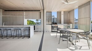 A modern kitchen with a central island, bar stools, and a dining area with a table and chairs. - Hastings Villas (Noosa Heads)