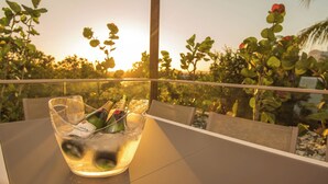 A table with a glass bowl containing bottles and glasses, set against a sunset view with greenery and a palm tree. - Hastings Villas (Noosa Heads)