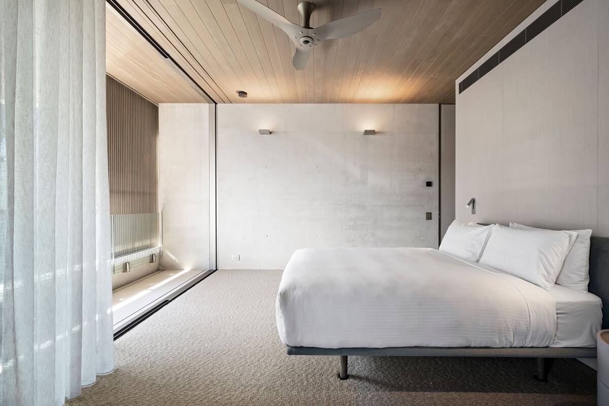 Um quarto moderno com uma cama grande, teto de madeira e uma janela com cortinas.