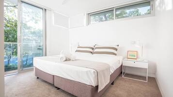 A modern bedroom with a large bed, a bedside table with a lamp, and a view of the outdoors through a sliding glass door.