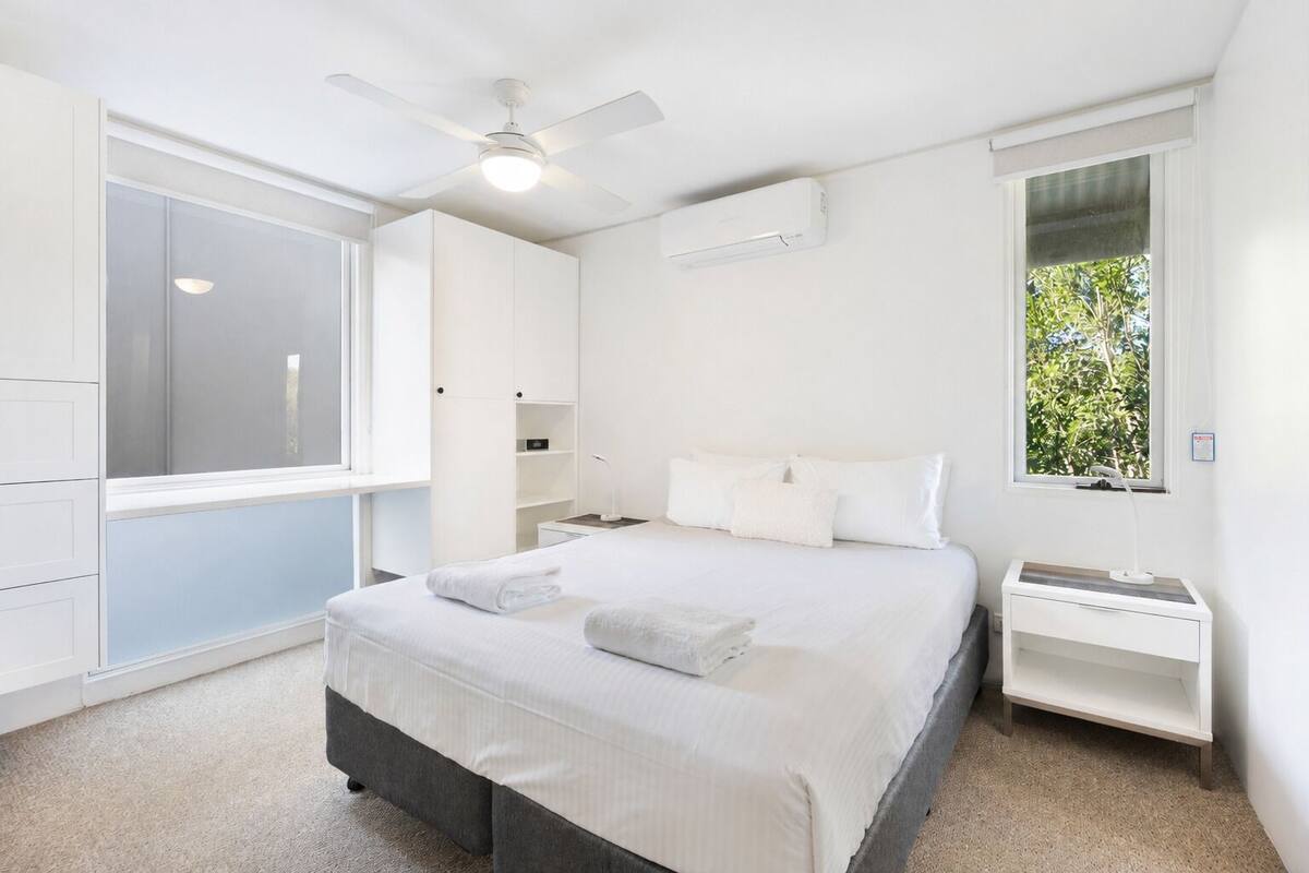 Quarto com cama, mesas de cabeceira, ventilador de teto, ar condicionado, janela com vista e guarda-roupa.