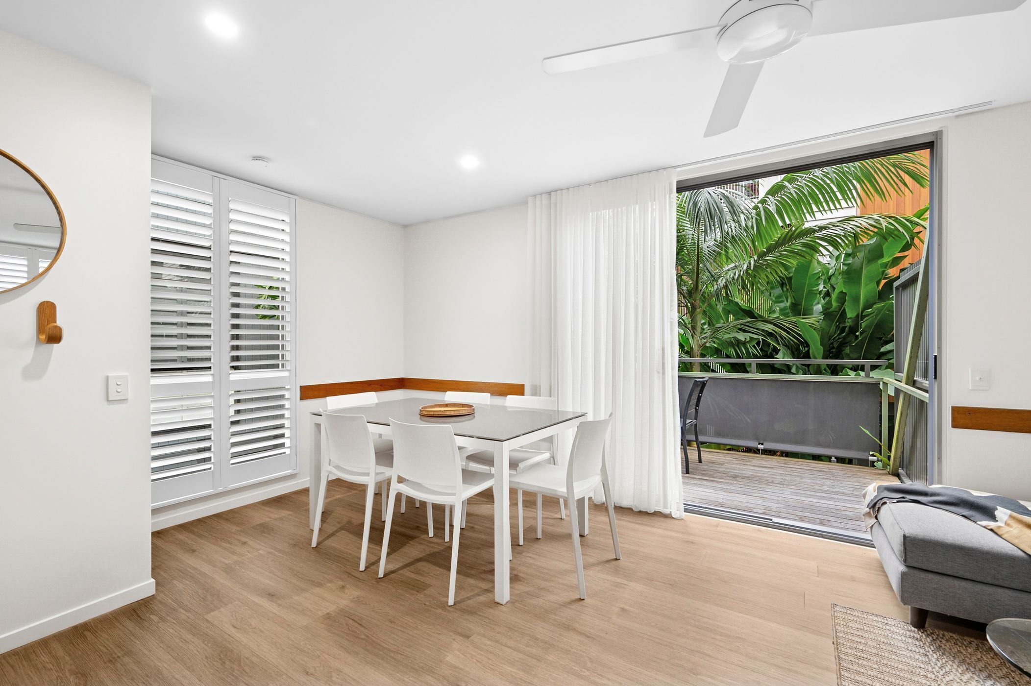 Un salón moderno con comedor, muebles blancos, un ventilador de techo y vistas a un balcón con plantas.