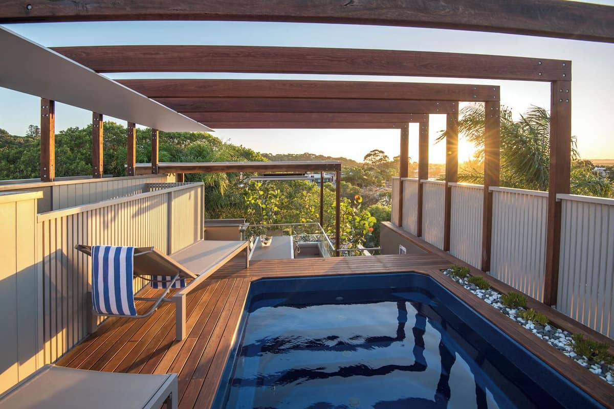 Um deck de madeira com uma banheira de hidromassagem, cadeiras de descanso e vista da paisagem ao redor.
