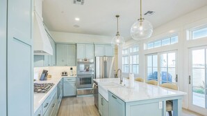 A modern kitchen with light blue cabinets, stainless steel appliances, a marble countertop, and pendant lighting.