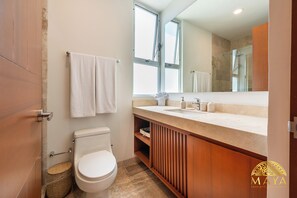 A modern bathroom with a toilet, a sink with a mirror, and a shower area. - NHOA 311A Lux 2BR Pool View Aldea Zama (Tulum)