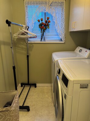 A laundry area with a washing machine, a drying rack, and a window with lace curtains. - New trailer with queen bed, air-con in Aldergrove, safe &quiet, privacy (Langley Township)