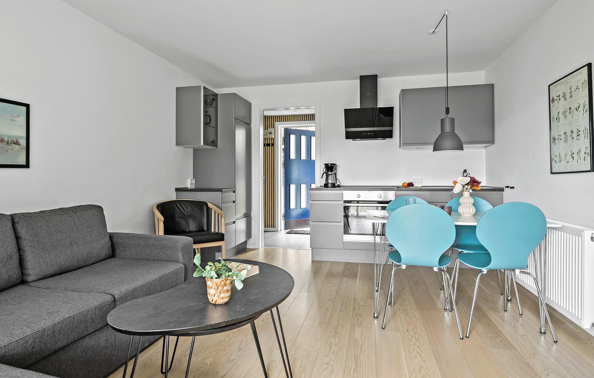 A modern living room with a grey sofa, a round coffee table with a plant, and a dining area with blue chairs and a white table.