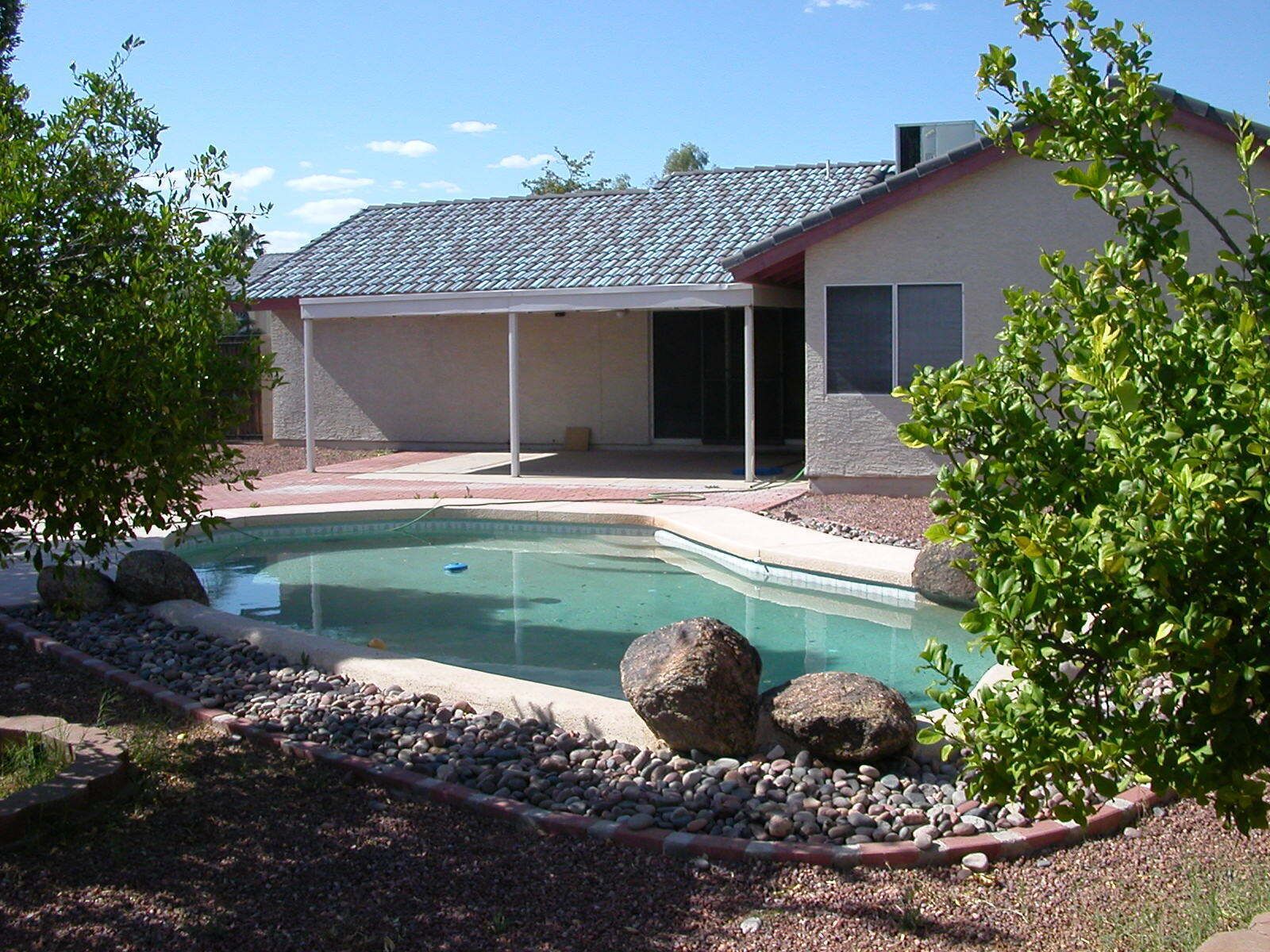 Un jardin à l’arrière d’une maison, avec une piscine, entouré de rochers et de verdure.