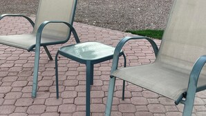 Kaksi ulkokäyttöön tarkoitettua metallituolia, joissa on verkkomainen selkänoja ja istuinosa, sijoitettu päällystetylle alueelle, jossa on kuusikulmaisia laattoja.