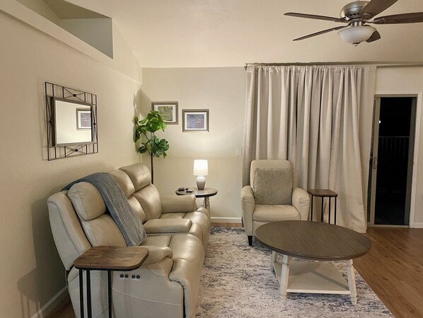 Una sala de estar con sofá, sillón, mesa de centro y ventilador de techo.