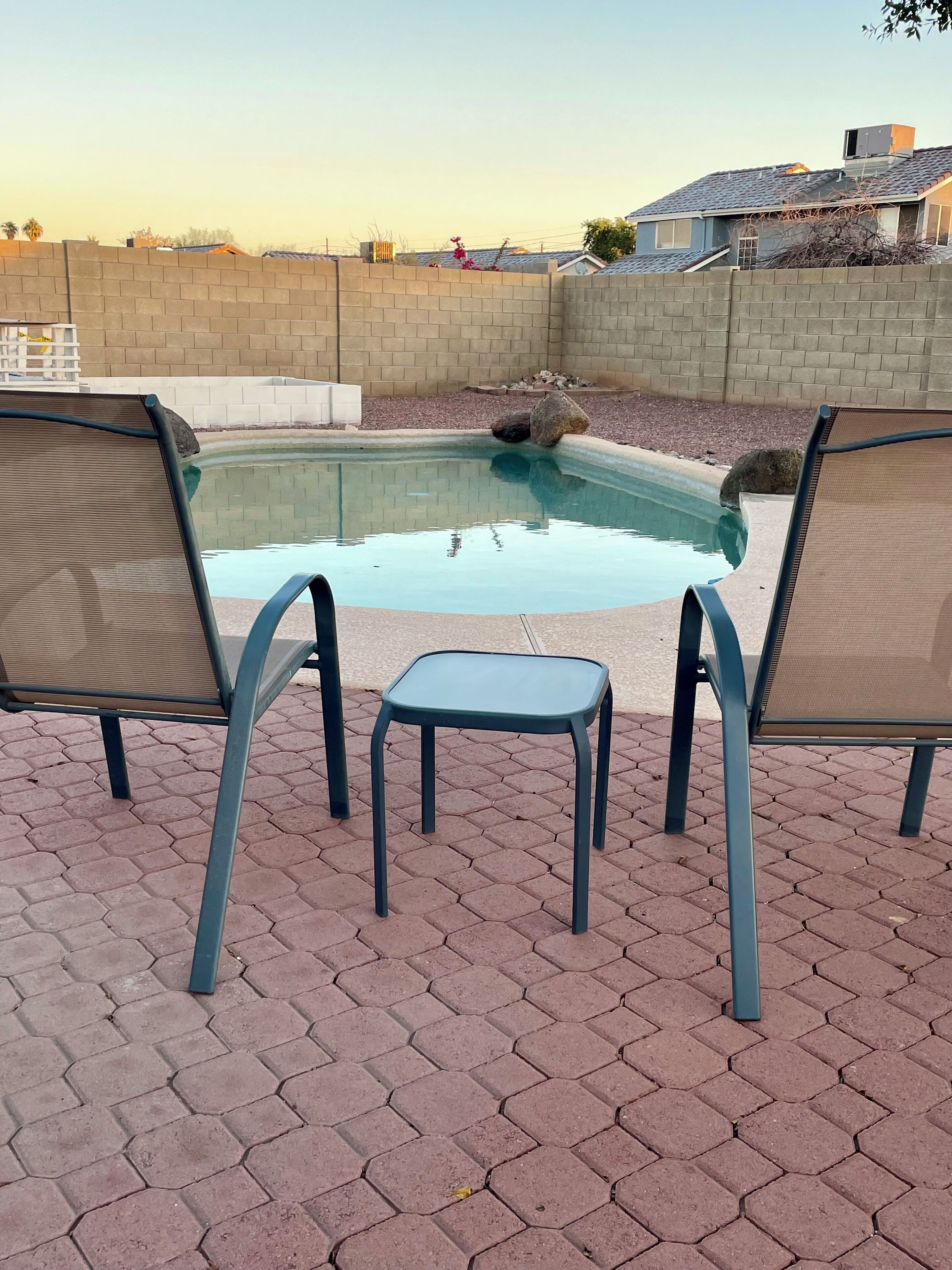 A pool area with two lounge chairs and a small table.