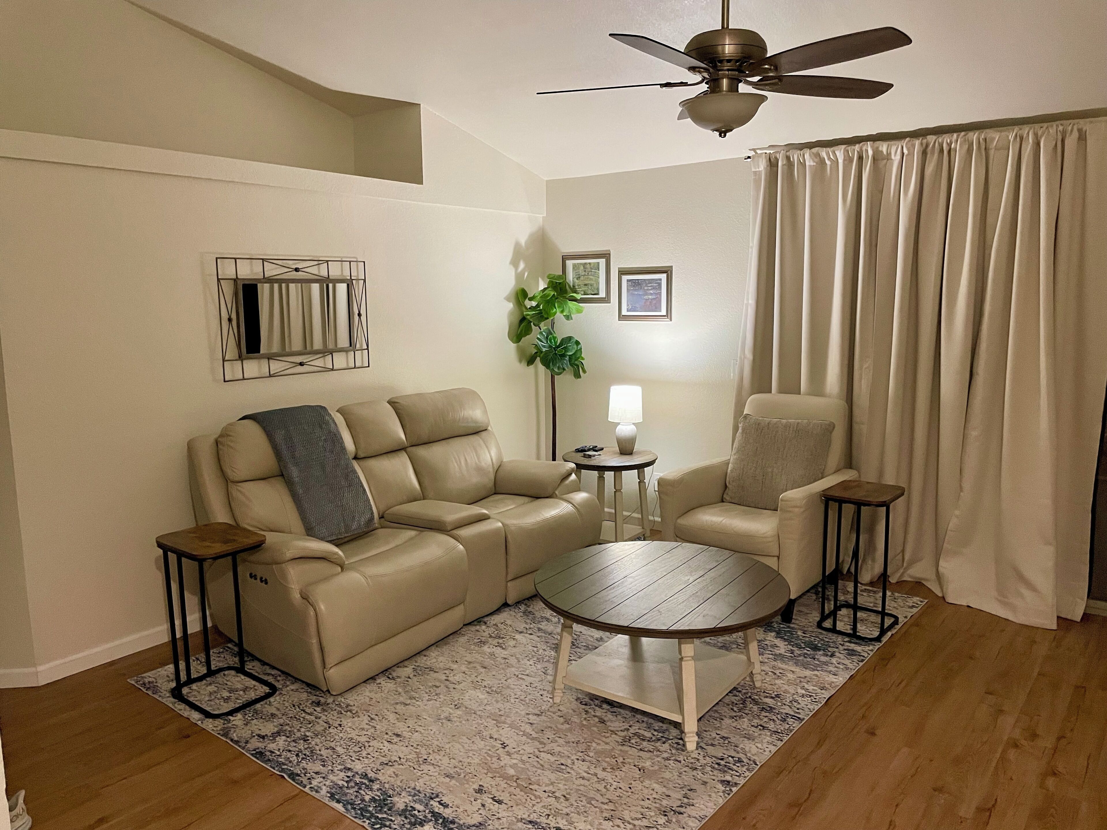 Un salon avec un canapé beige, une table basse ronde, une table d’appoint, un lampadaire et un ventilateur de plafond.