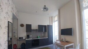 Een compacte hotelkamer met een bed, een klein kitchenette, een bureau met stoel en een televisie.