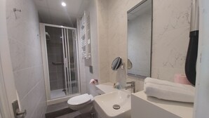 Een moderne badkamer met een douchecabine van glas, een toilet, een wastafel en een spiegel.