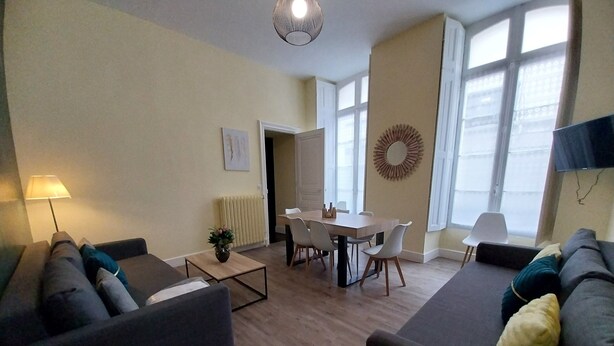 A modern living room with a sofa, a coffee table, and a dining area with chairs and a table. - Apartment T2+ ( sleeps 3 ) (Bagnères de Luchon)