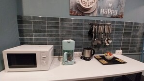 A kitchen with a microwave, coffee maker, and kettle on the counter. There are utensils hanging on the wall and a sign that says "Be Happy". - Apartment T2+ ( sleeps 3 ) (Bagnères de Luchon)