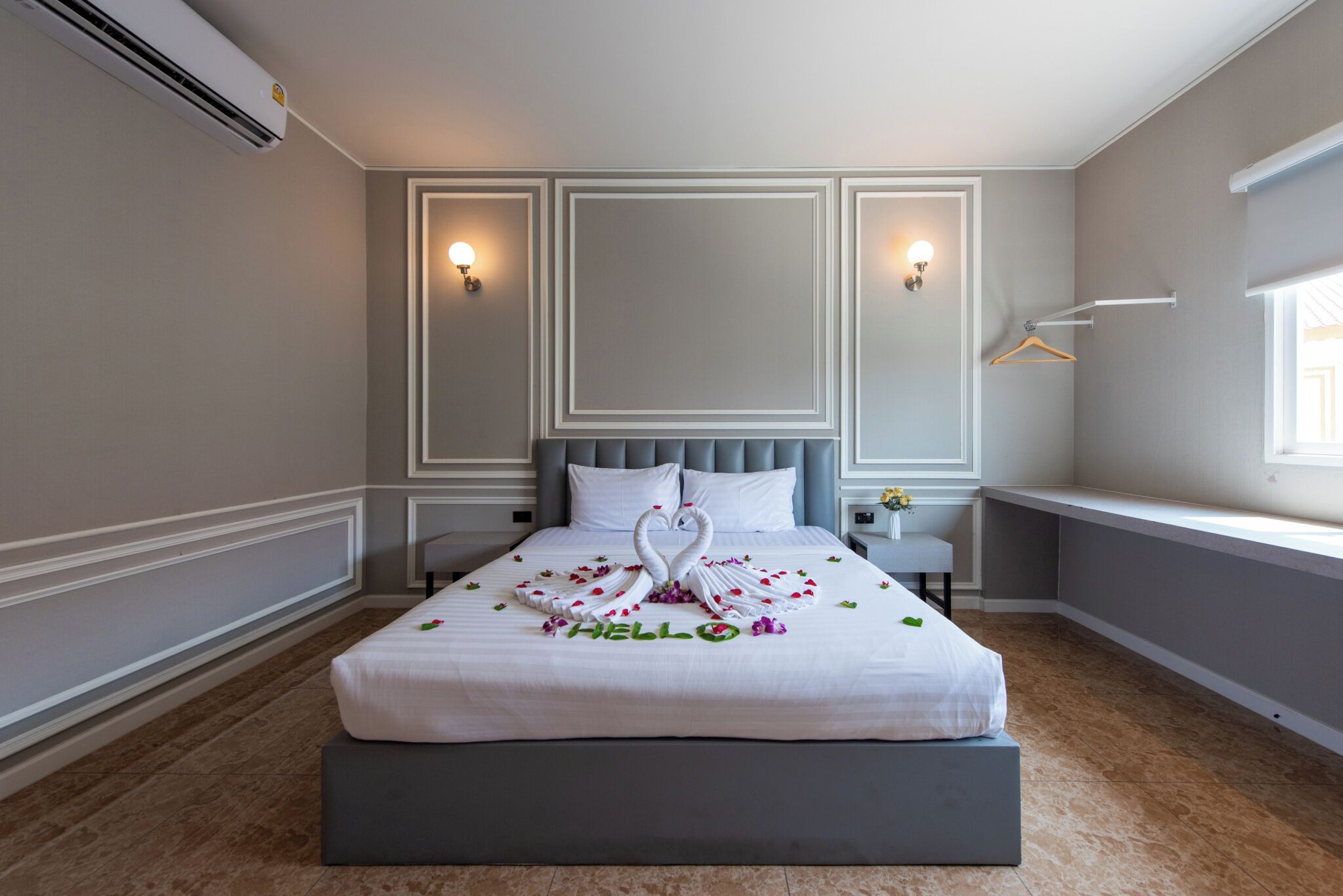 A neatly made bed with a swan and rose decoration, a bedside table with a lamp, and a window with a view.