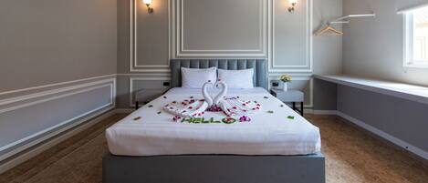 A neatly made bed with a swan and rose decoration, a bedside table with a lamp, and a window with a view.
