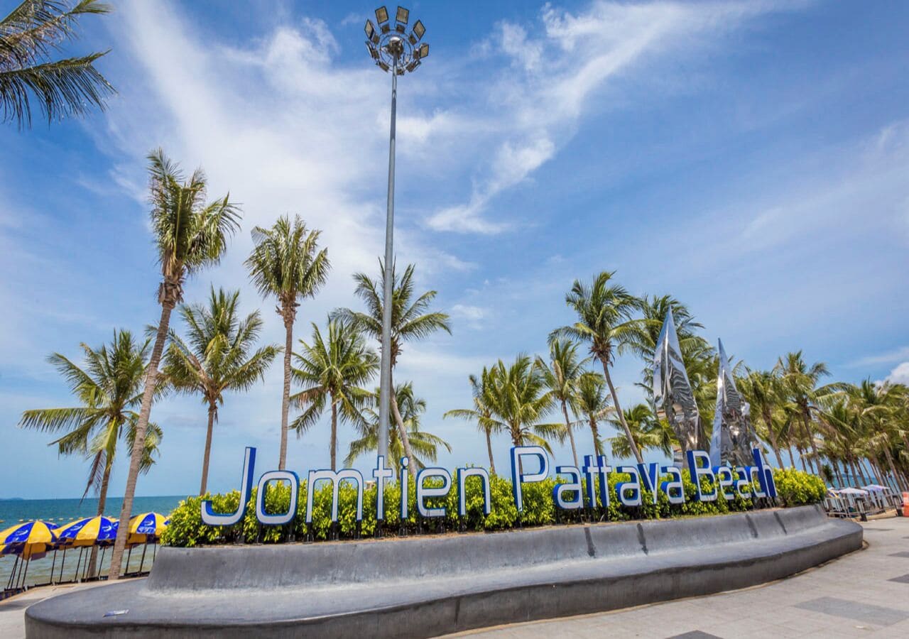 Een strand met palmbomen, een bord waarop 'Jonmten Pattaya Beach' staat en een lantaarn.
