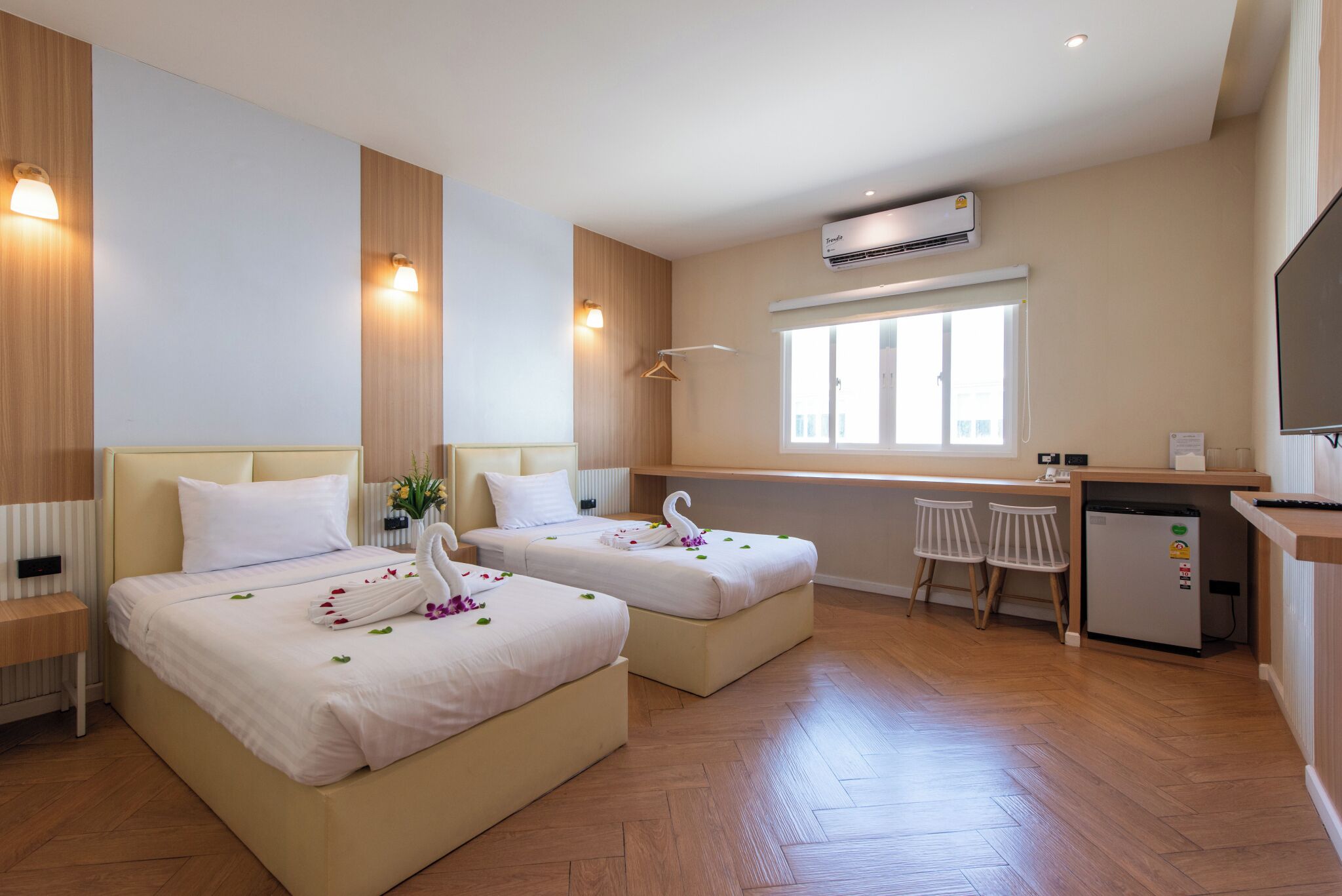 A hotel room with two beds, a kitchenette, a small desk, and a window.