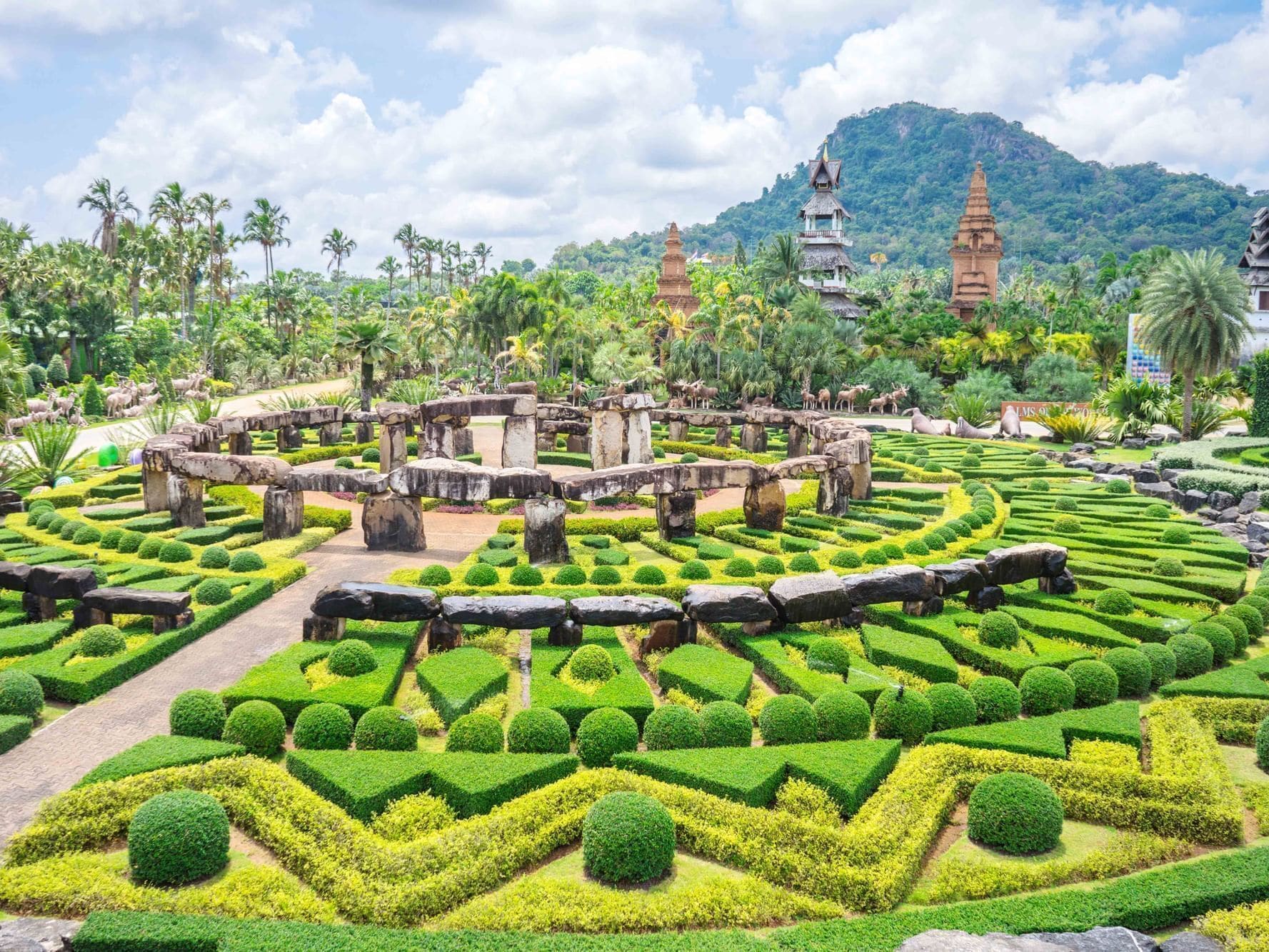 A well-maintained garden with geometric hedges, stone structures, and traditional architecture in the background.