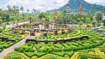 A well-maintained garden with geometric hedges, stone structures, and traditional architecture in the background.