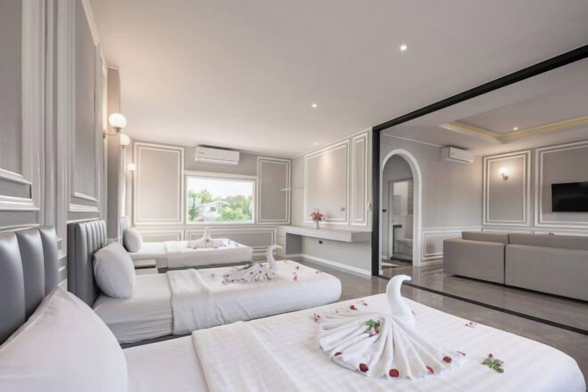 A hotel room with two beds, a sofa, a TV, and a view of greenery outside.