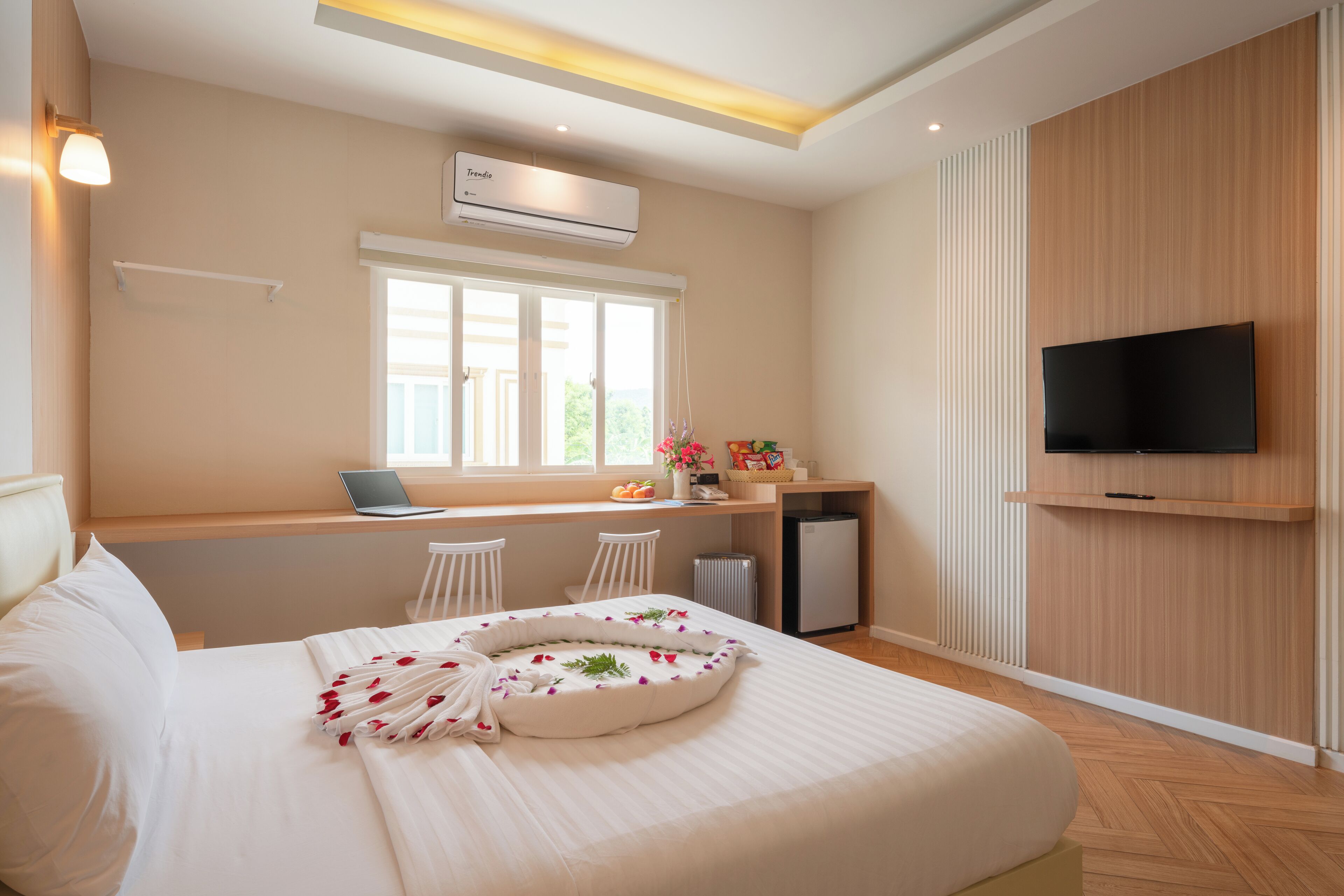 Una habitación de hotel moderna con una cama, un escritorio con una computadora portátil, un televisor y un aire acondicionado.