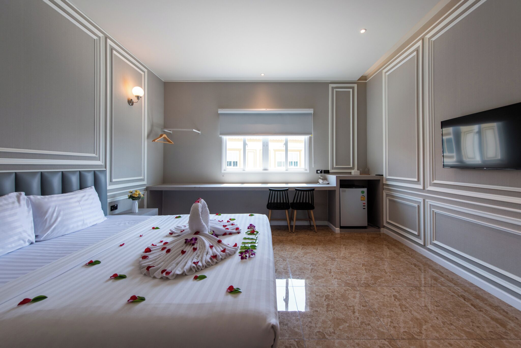 A hotel room with a bed, a desk, a chair, a TV, and a window.