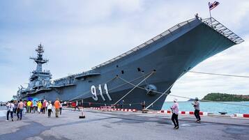 A large naval ship docked at a port with people walking around.