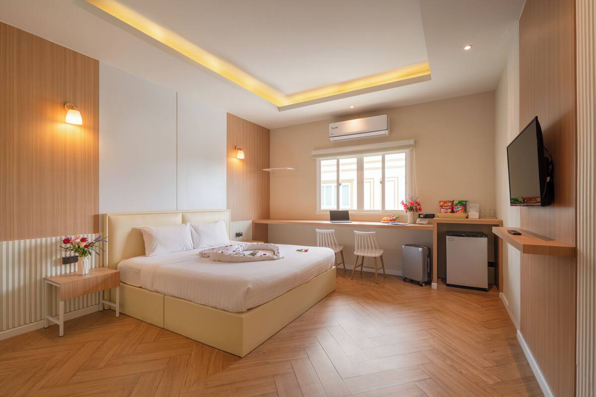 A modern hotel room with a large bed, a desk, a television, and a small refrigerator.
