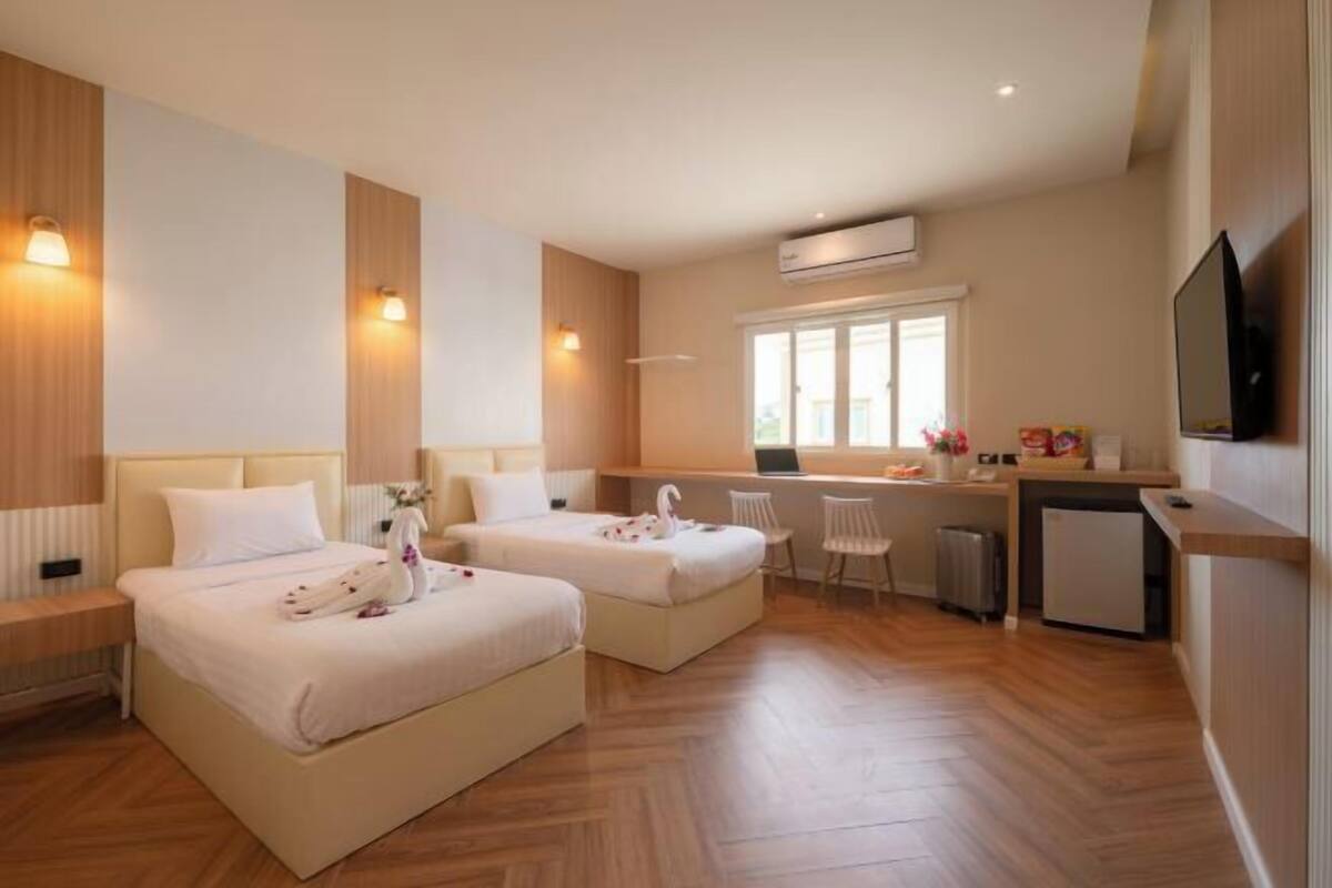 A hotel room with two beds, a desk, a chair, a TV, and a kitchenette.
