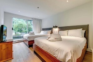 A hotel room with two beds, a television, and a large window with a view of trees.