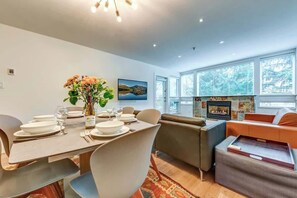 A modern dining area with a table set for four, a sofa, and a fireplace. - Greystone Lodge 102 Ski-in/Out by Acer Vacations (Whistler)