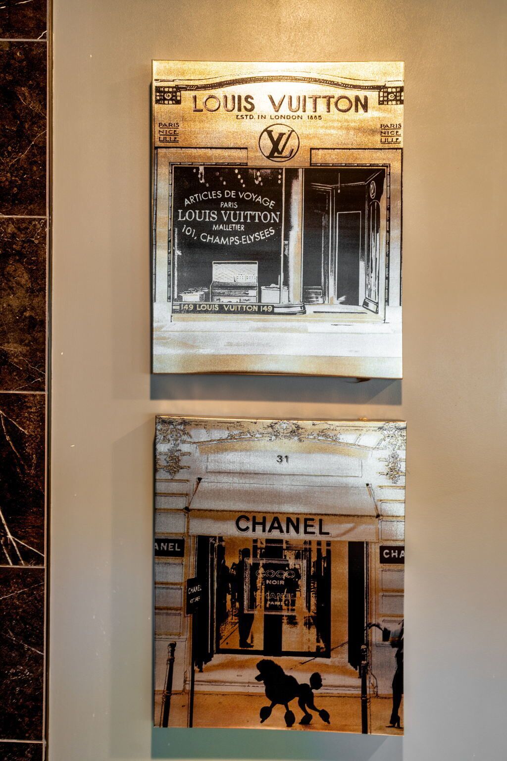 Two posters of storefronts, one for Louis Vuitton and one for Chanel, on a wall.