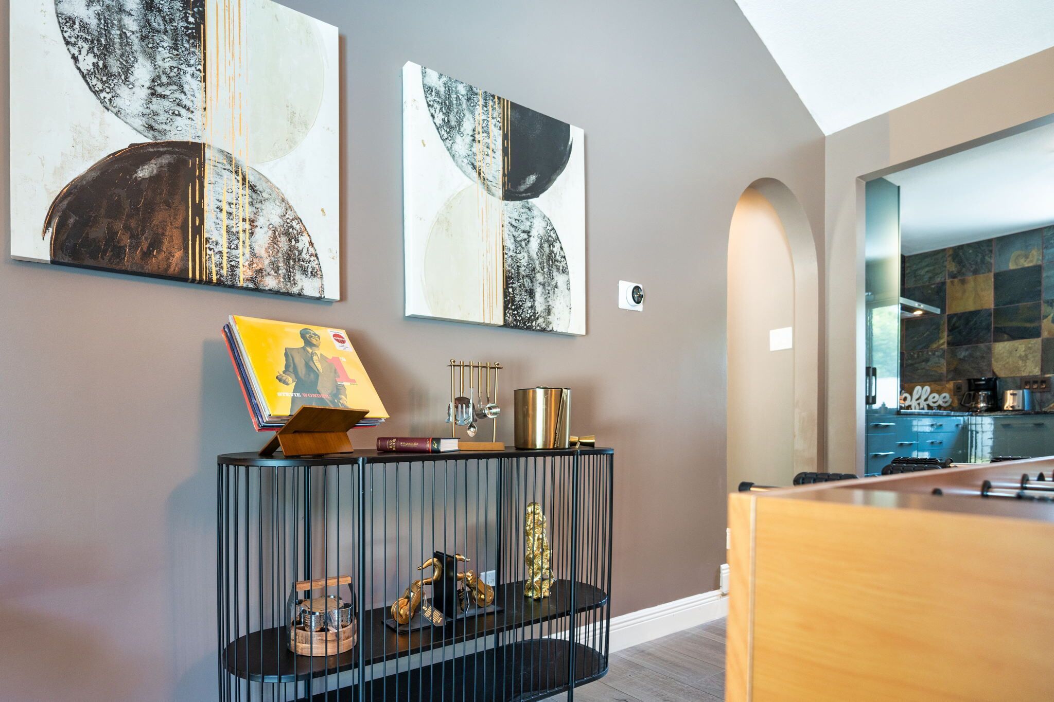 A modern living room with abstract wall art, a console table with decorative items, and a view into the kitchen.